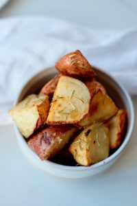 a bowl of rosemary and garlic roasted potatoes sitting on a white table with a white towel