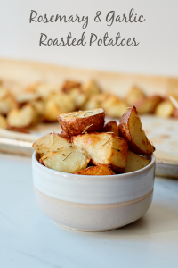 Rosemary & Garlic Roasted potatoes in a bowl sitting in front of a baking sheet with more potatoes
