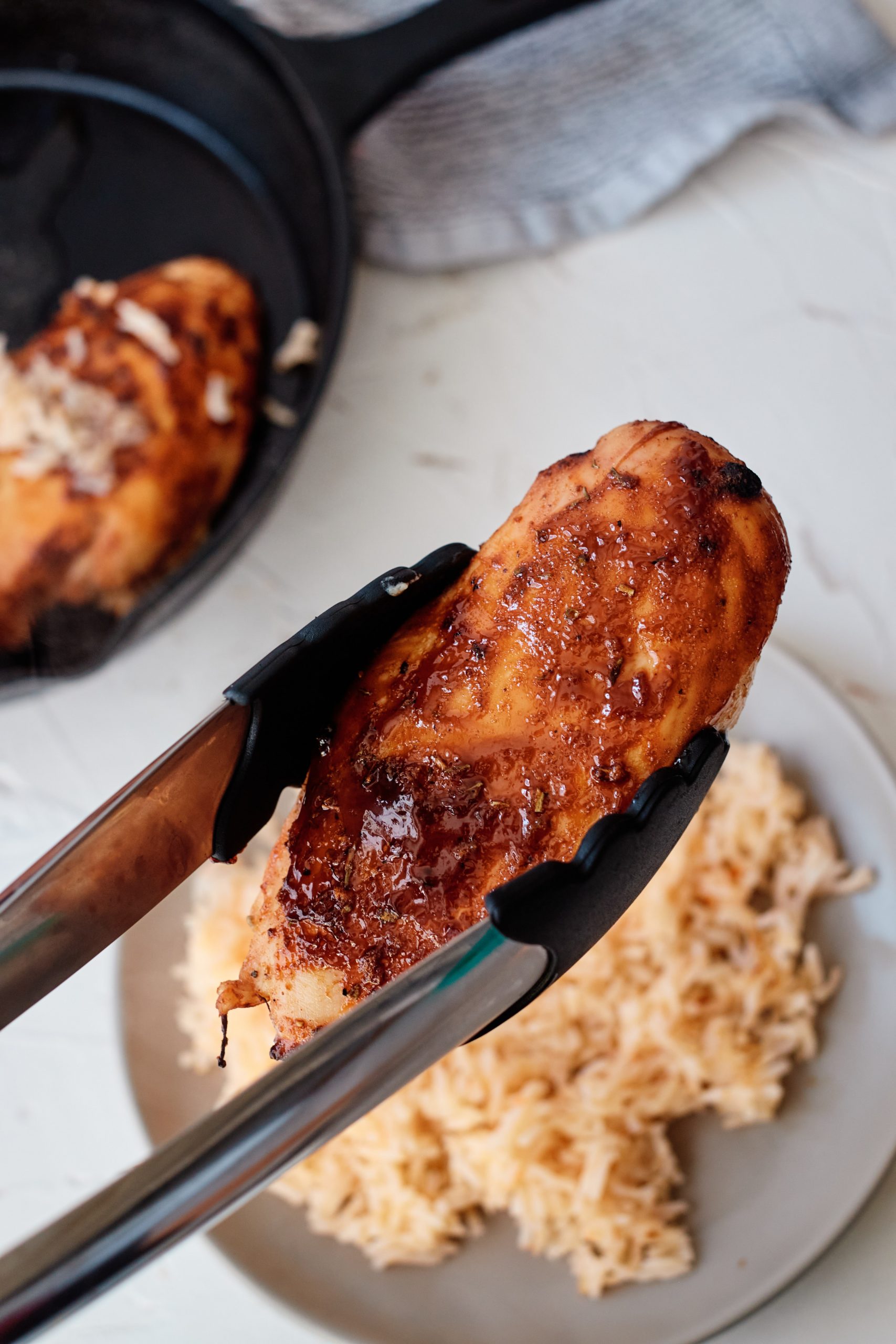 Cuban-Style Sautéed Chicken held by tongs being set down on a plate on top of rice