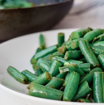White plate filled with stir-fry green beans with a sauce pan in the background