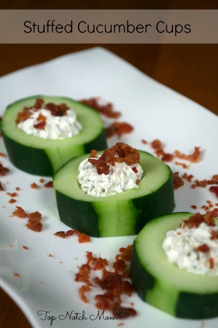 Three Stuffed Cucumber Cups sitting on a white plate. Filled with herb cream cheese stuffing and topped with crumbled bacon