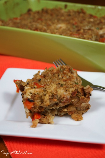 A portion of Stuffing Casserole on a white plate with a green baking dish in the background filled with the casserole