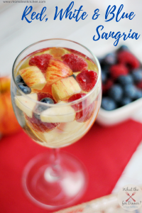 Wine glass of sangria filled with blueberries, raspberries and diced apples, sitting on a red napkin next to a bowl of mixed berries