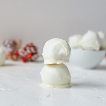 two truffles stacked on each other in front of a white bowl full of truffles with Christmas decorations in the background