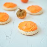Four Vanilla Pumpkin Cookies on a white table with small pumpkins in the background