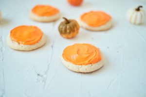 Four Vanilla Pumpkin Cookies on a white table with small pumpkins in the background