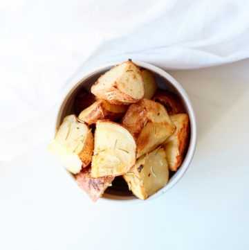 a white bowl of Rosemary & Garlic Roasted Potatoes sitting on a white table