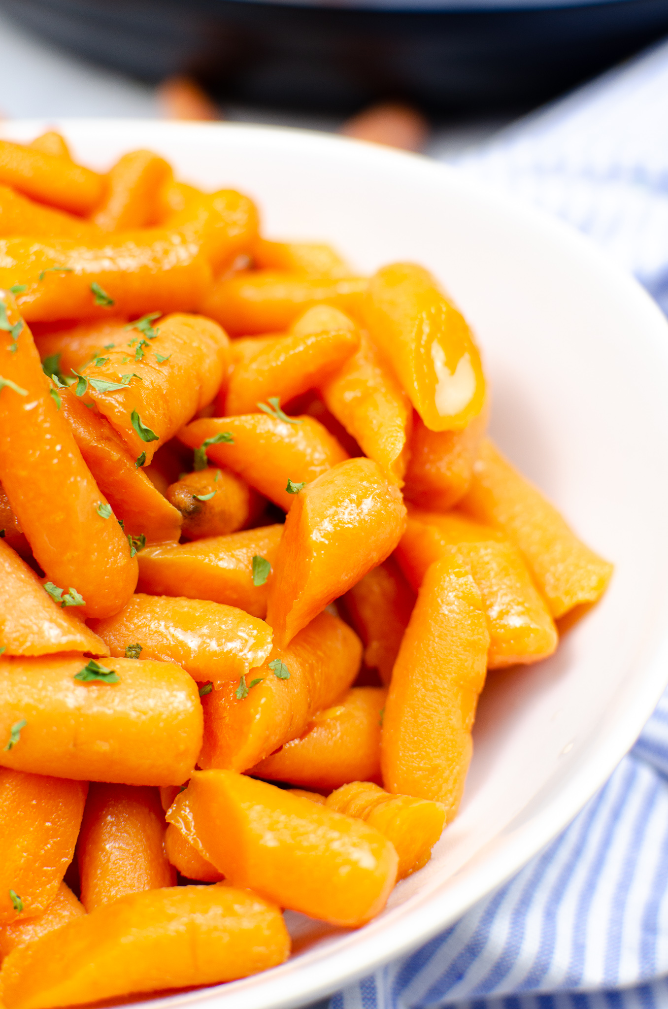 unclose photo of a white bowl filled with brown sugar glazed carrots, topped with parsley