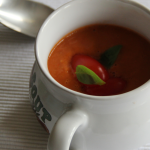 a white soup mug filled with tomato soup with a silver spoon