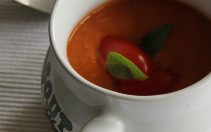 a white soup mug filled with tomato soup with a silver spoon
