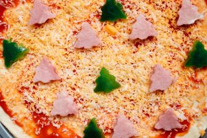 Christmas tree shaped ham and green pepper slices topped on a pizza ready to be baked