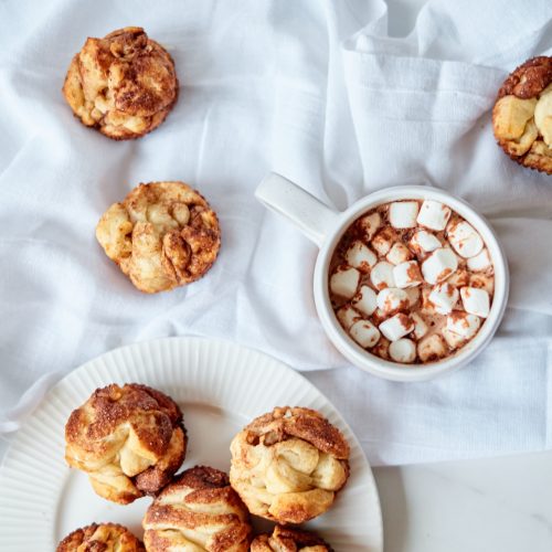 Monkey Bread Muffins sitting on a white towel next to a mug full of hot chocolate