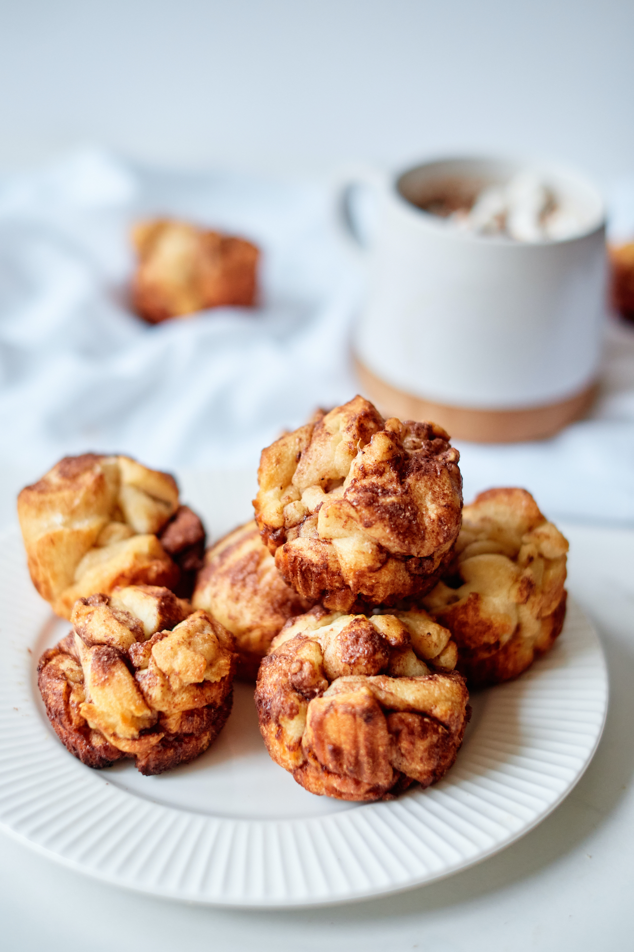 a white plate filled with 6 Monkey Bread Muffins sitting in front of a white mug of hot chocolate