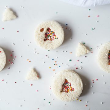 four Christmas Uncrustables on a white table with extra Christmas trees made from bread and sprinkles around them