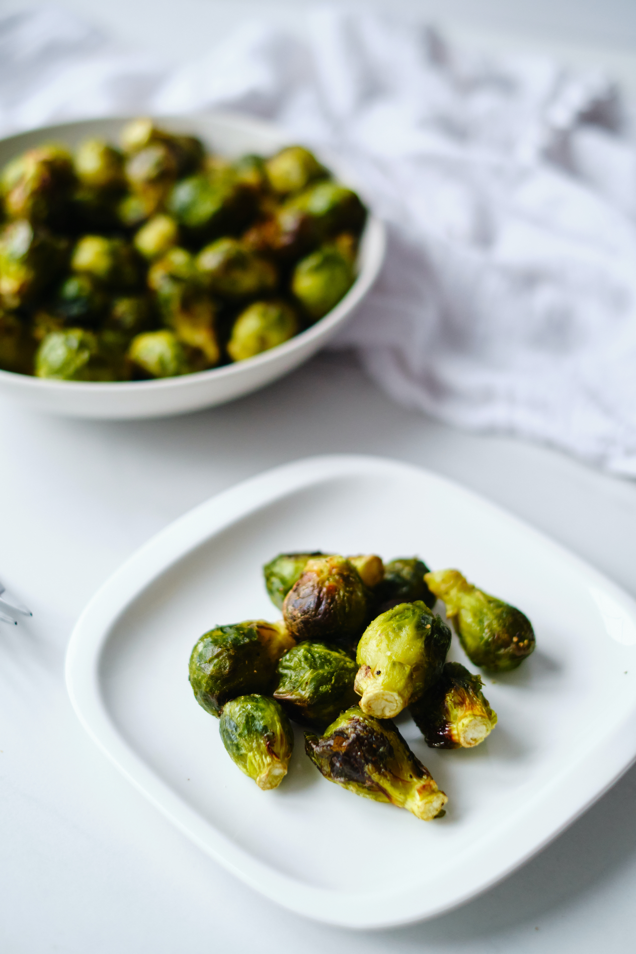 a white plate with a serving of air fryer Brussels sprouts with a full bowl in the background
