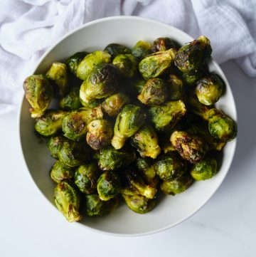 a white bowl filled with air fryer Brussels sprouts sitting next to a white kitchen towel