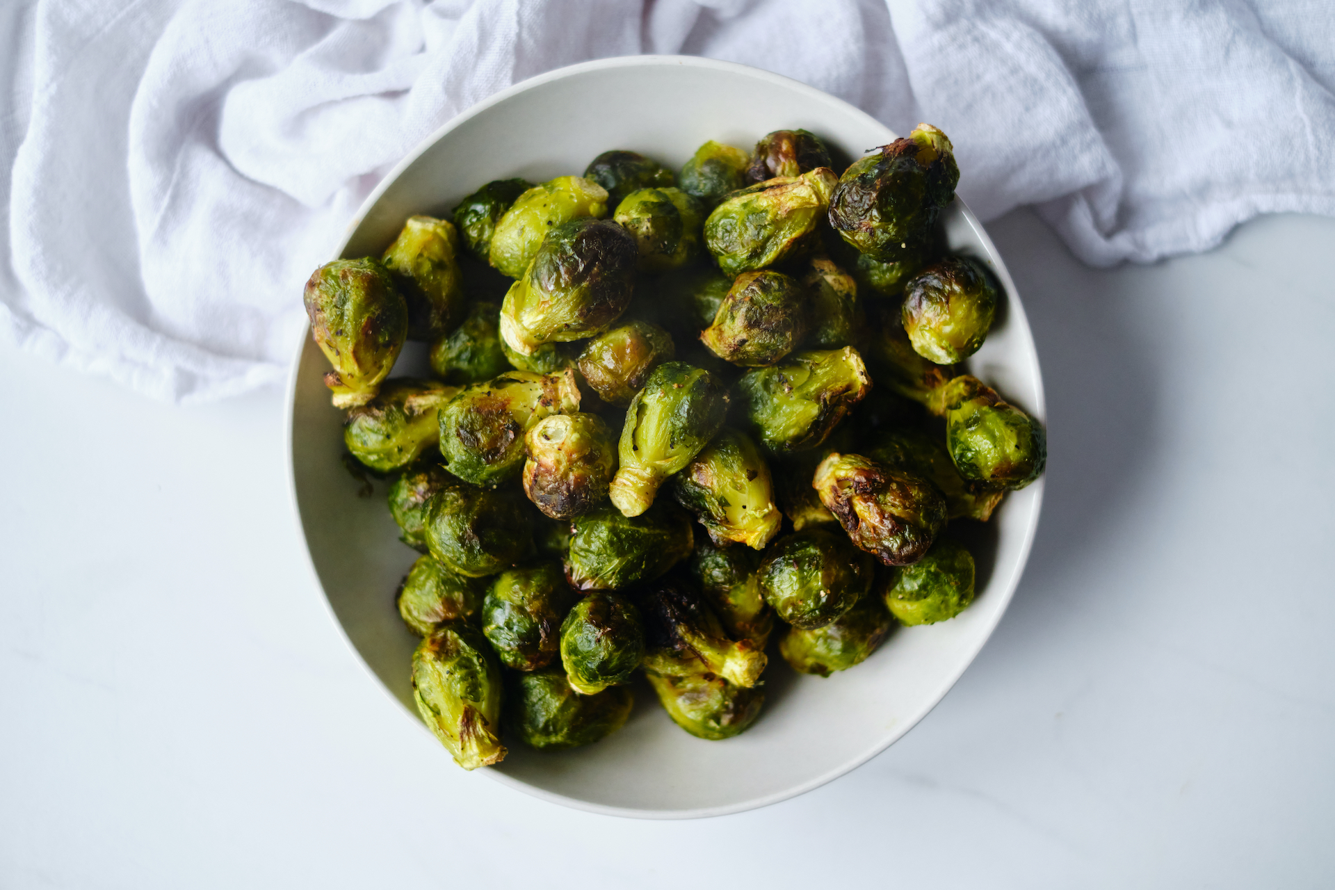 a white bowl filled with air fryer Brussels sprouts sitting next to a white kitchen towel