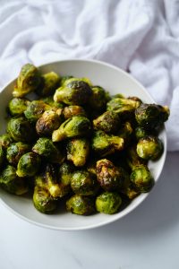 a white bowl filled with air fryer Brussels sprouts sitting next to a white kitchen towel