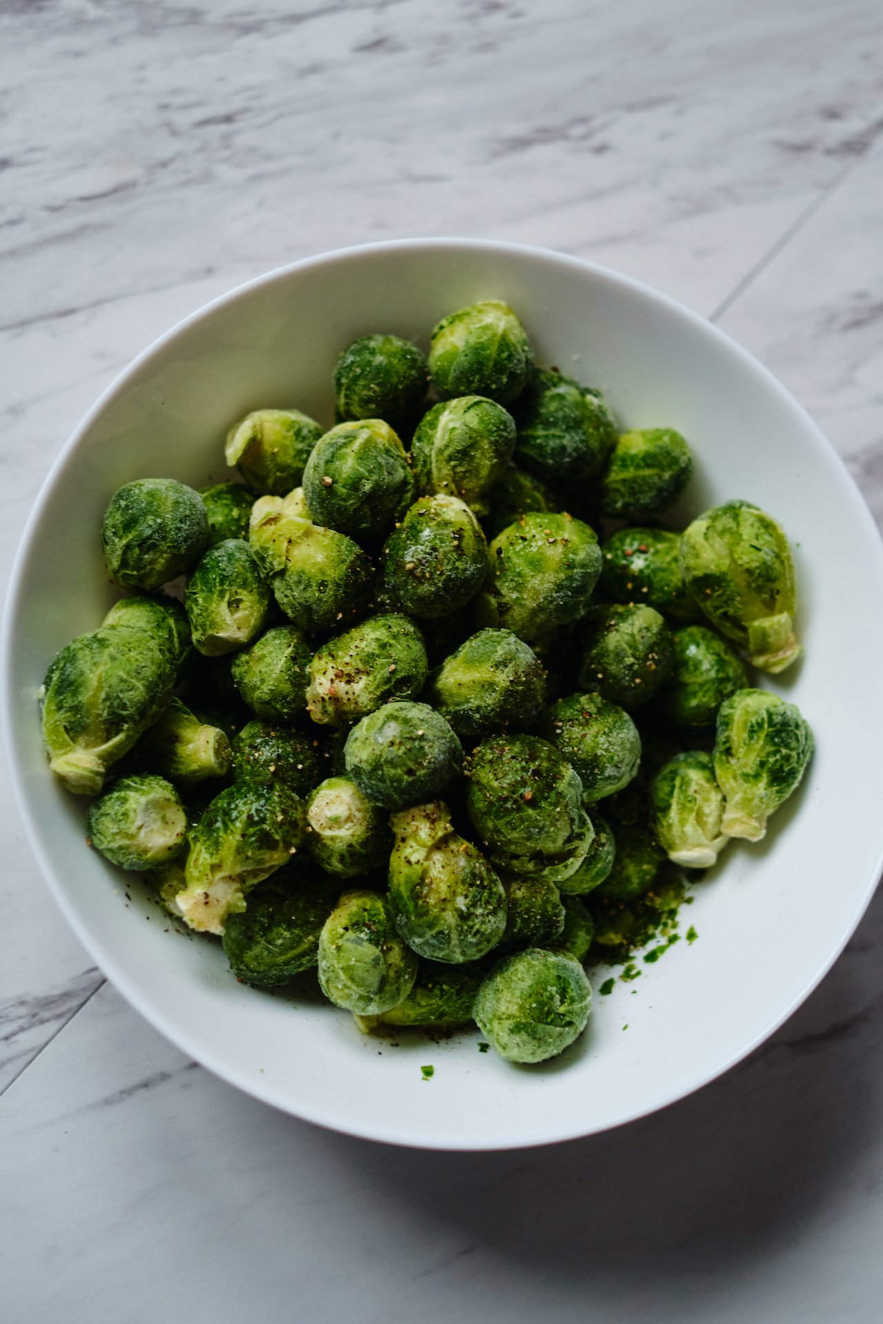 sprouts prior to be cooked in a white bowl seasoned with oil, salt and pepper