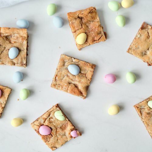 seven mini egg cookie bars sitting on a white background surrounded by mini egg candies
