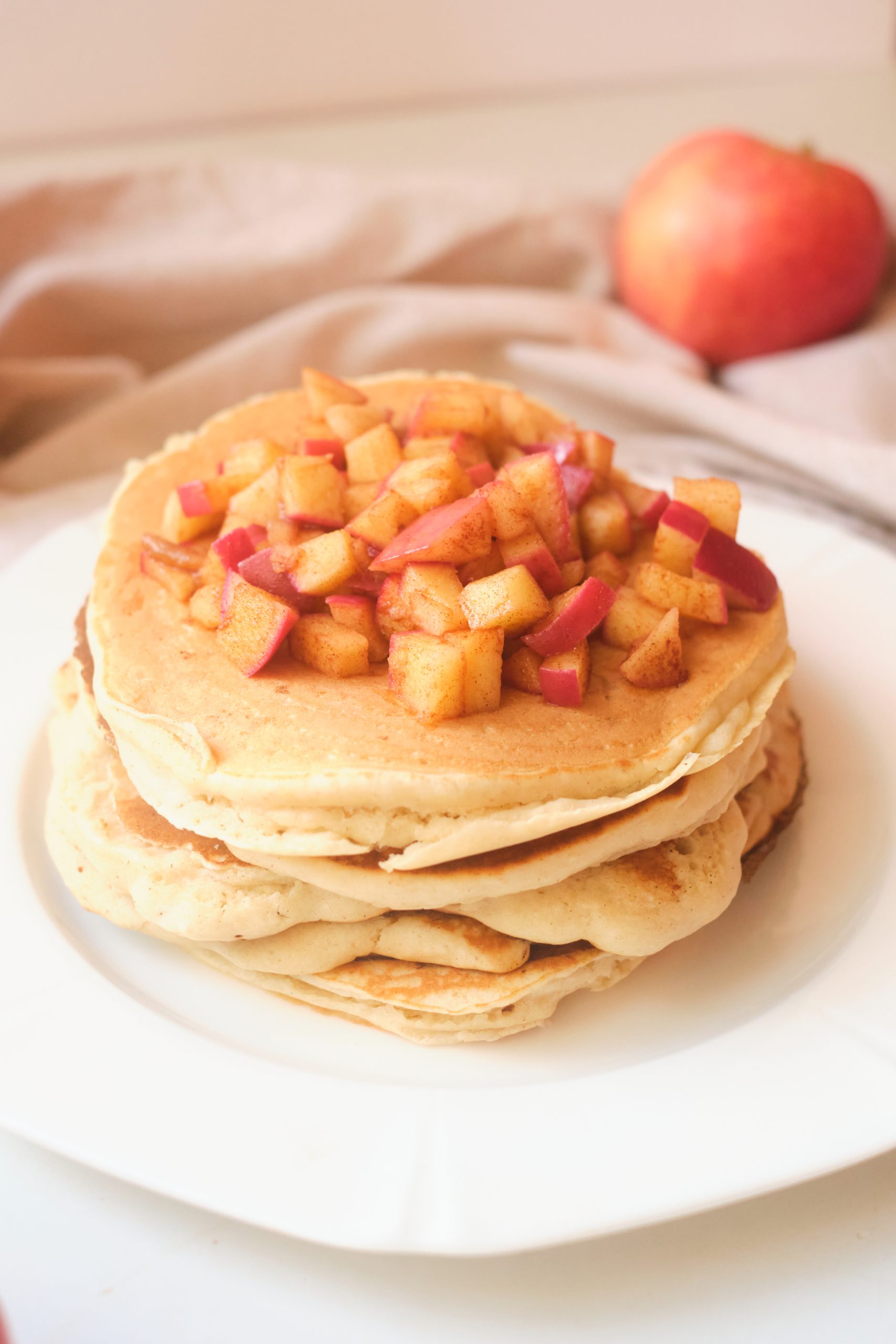 apple butter pancakes stacked on a white plate. Topped with diced cinnamon sugar apples.