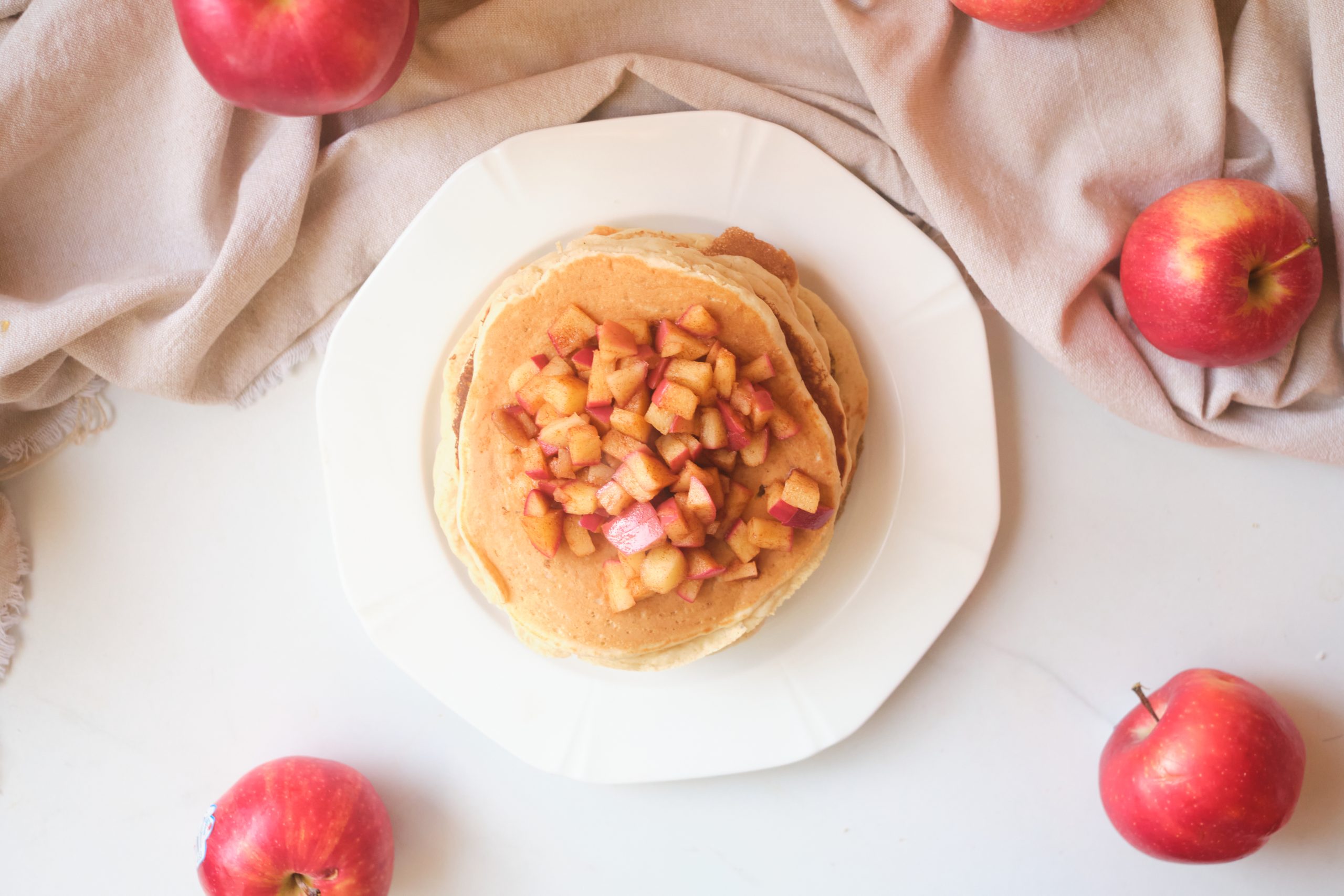 top view of pancakes topped with diced apples sitting on a white plate