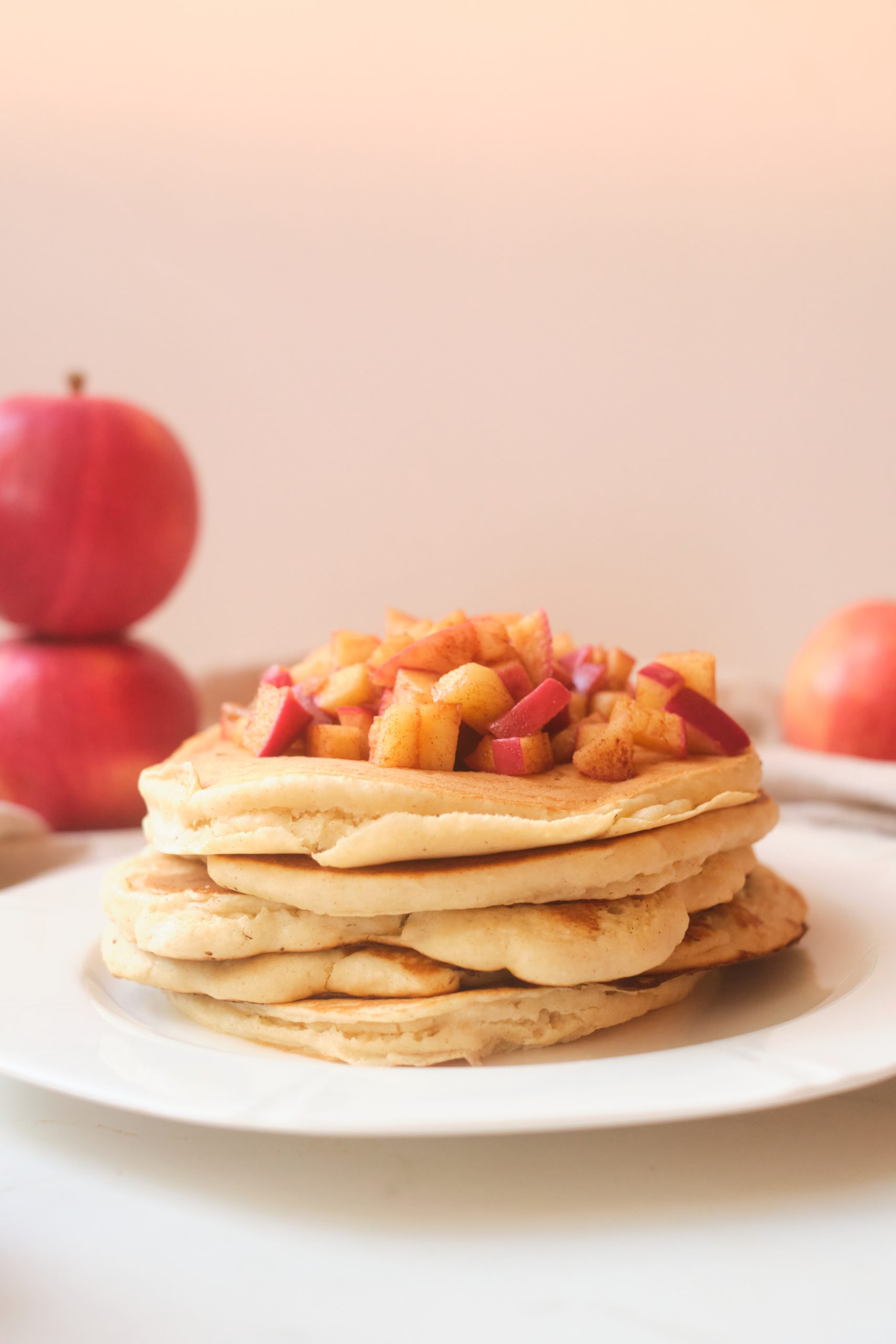 a stack of apple butter pancakes sitting on a white plate, topped with diced cinnamon fried apples.