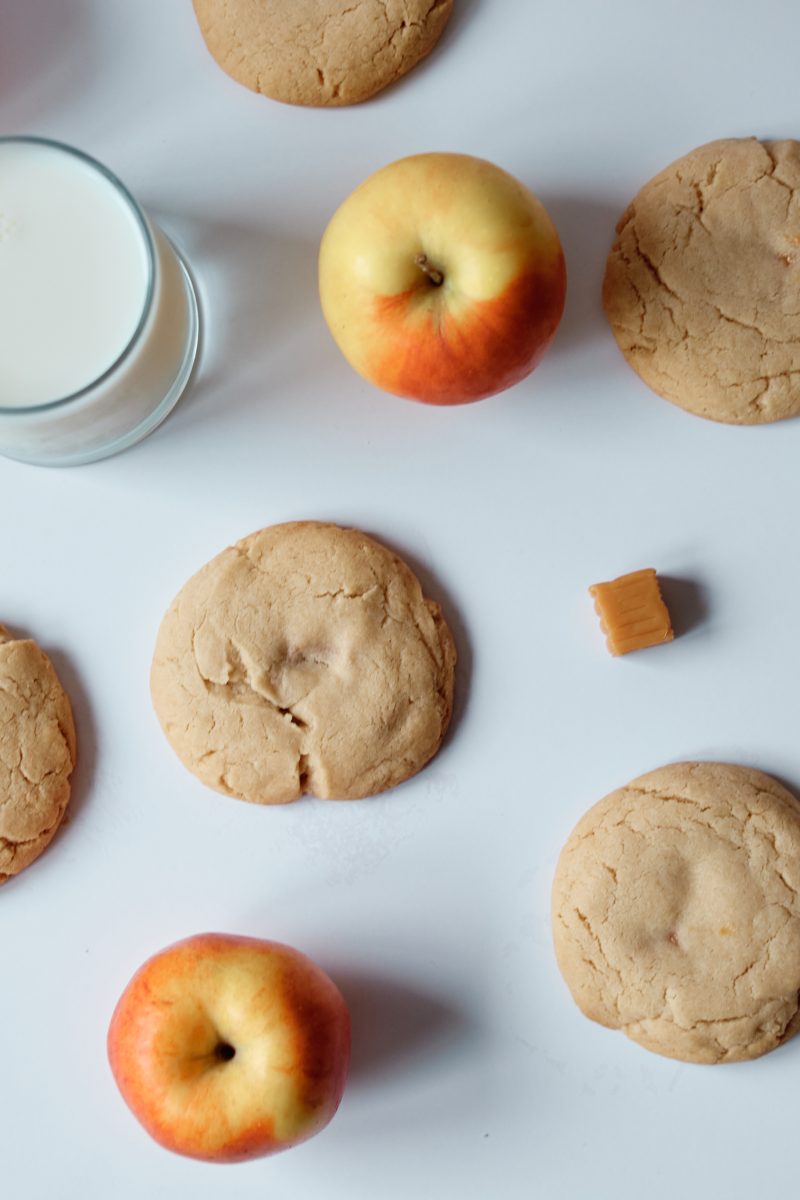 five cookies laying on a table with a whole red apple and caramel squares